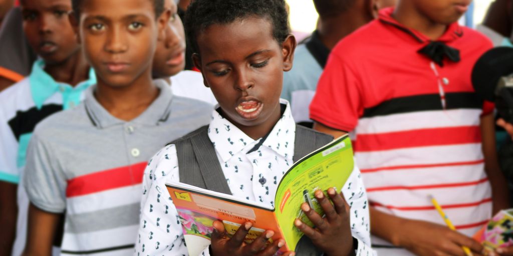 man in red and white polo shirt holding yellow book