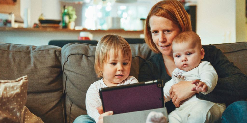 two babies and woman sitting on sofa while holding baby and watching on tablet