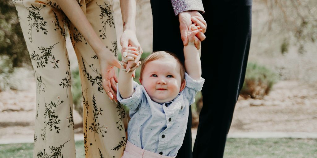 man and woman holding hand of toddler walking on grass field